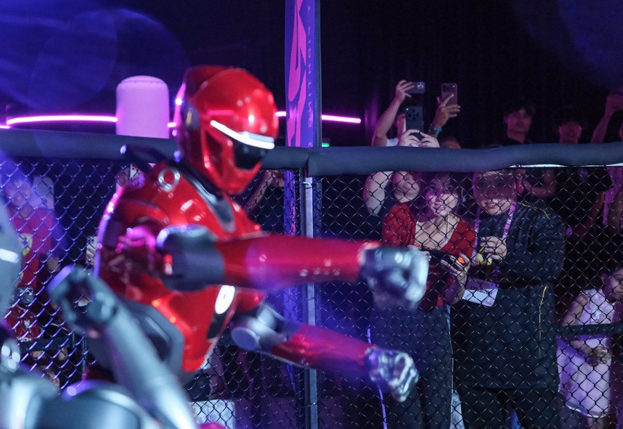 Red RFC robot throwing a punch against the cage wall while the crowd films